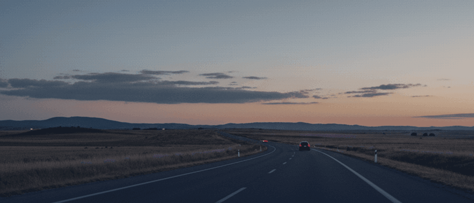 Atardecer en autovía española camino a Valencia con un coche eléctrico circulando hacia el horizonte — montañas, cielo cálido y carretera abierta